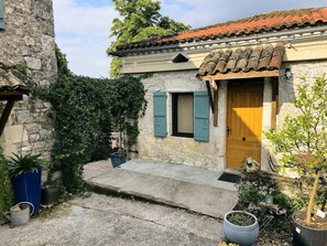 Un bâtiment rustique en pierre, avec un toit en tuiles, une porte en bois et une petite fenêtre avec des volets.
