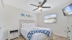 Une chambre à coucher avec un lit, un ventilateur de plafond, une fenêtre et des œuvres d’art accrochées au mur.