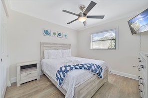 Une chambre à coucher avec un lit, un ventilateur de plafond, une fenêtre et des œuvres d’art accrochées au mur.