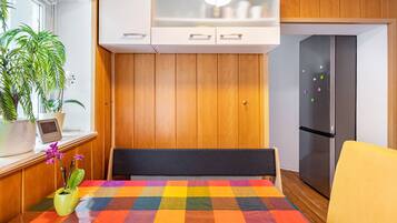 A kitchen with wooden cabinets, a refrigerator, a colorful table, and a potted plant.