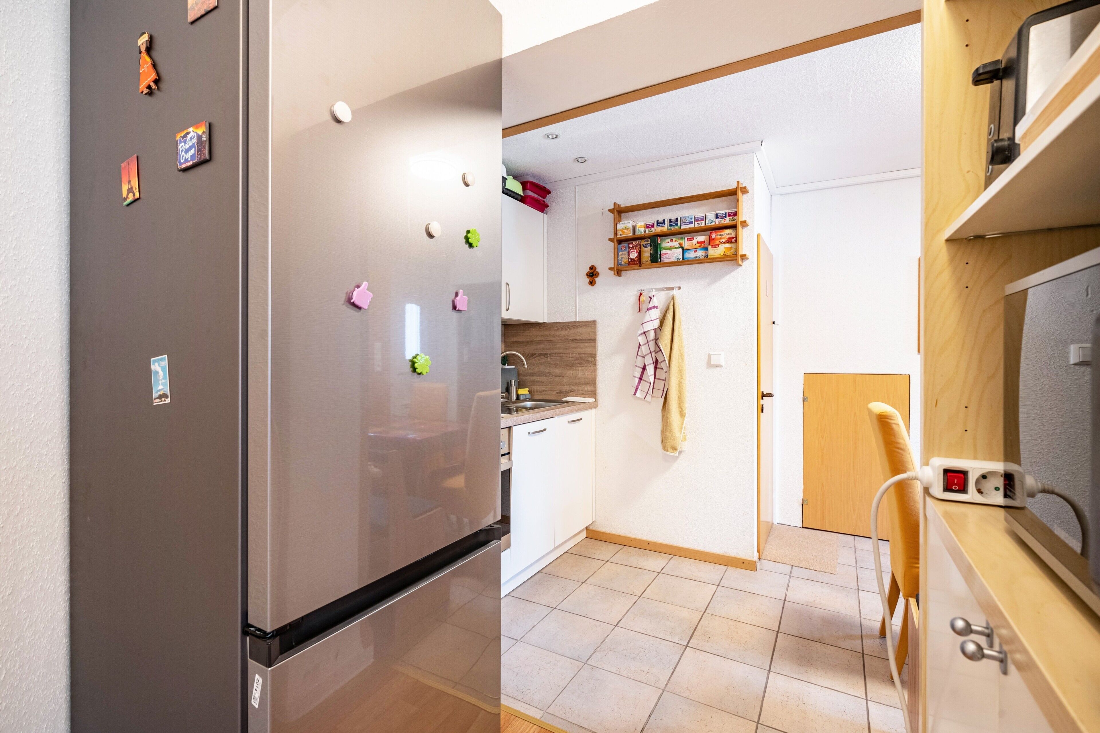 Eine Küche mit Kühlschrank, einem Holzregal und einem Handtuch an der Wand.