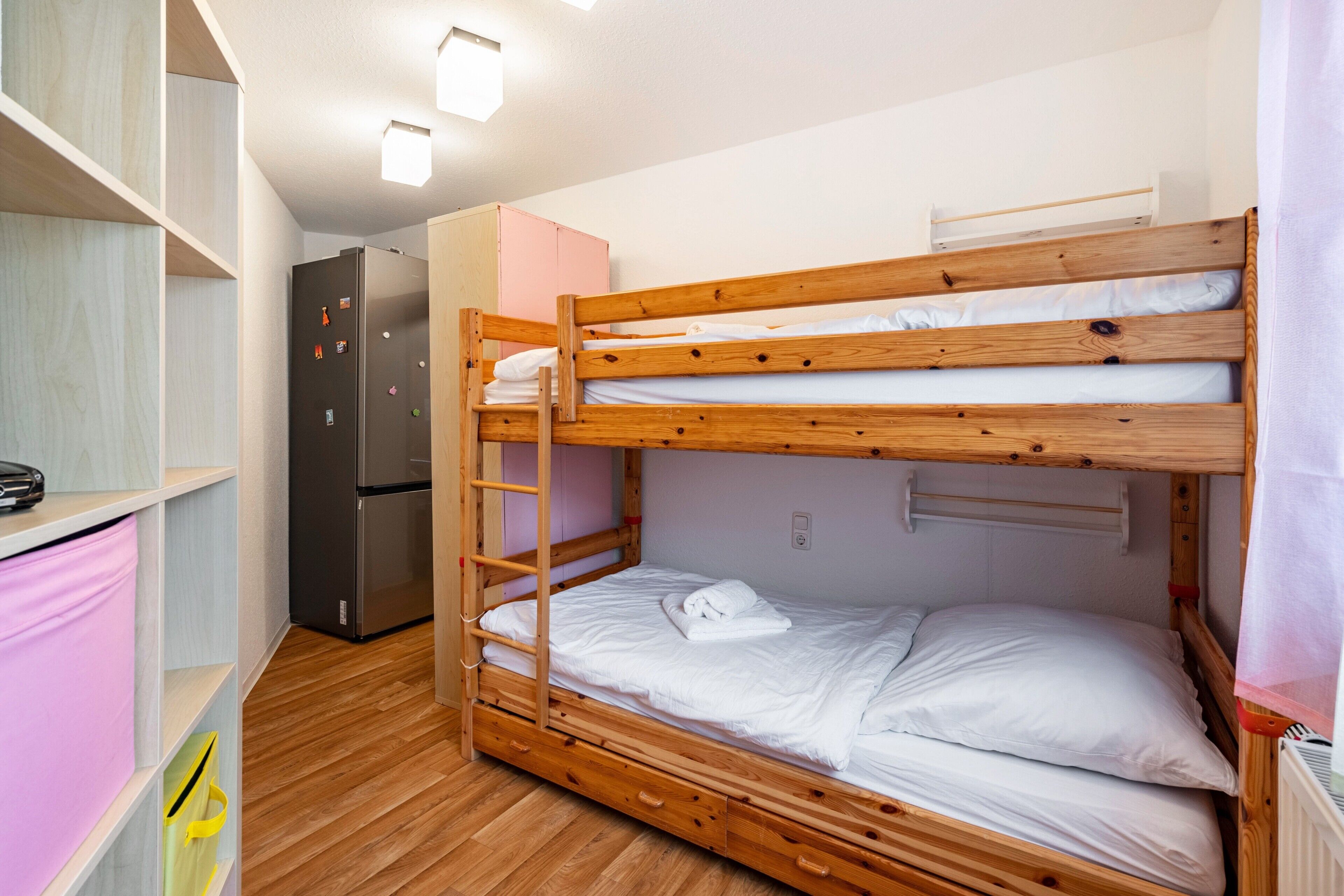 A bunk bed room with a wooden floor, a refrigerator, and a pink cabinet.