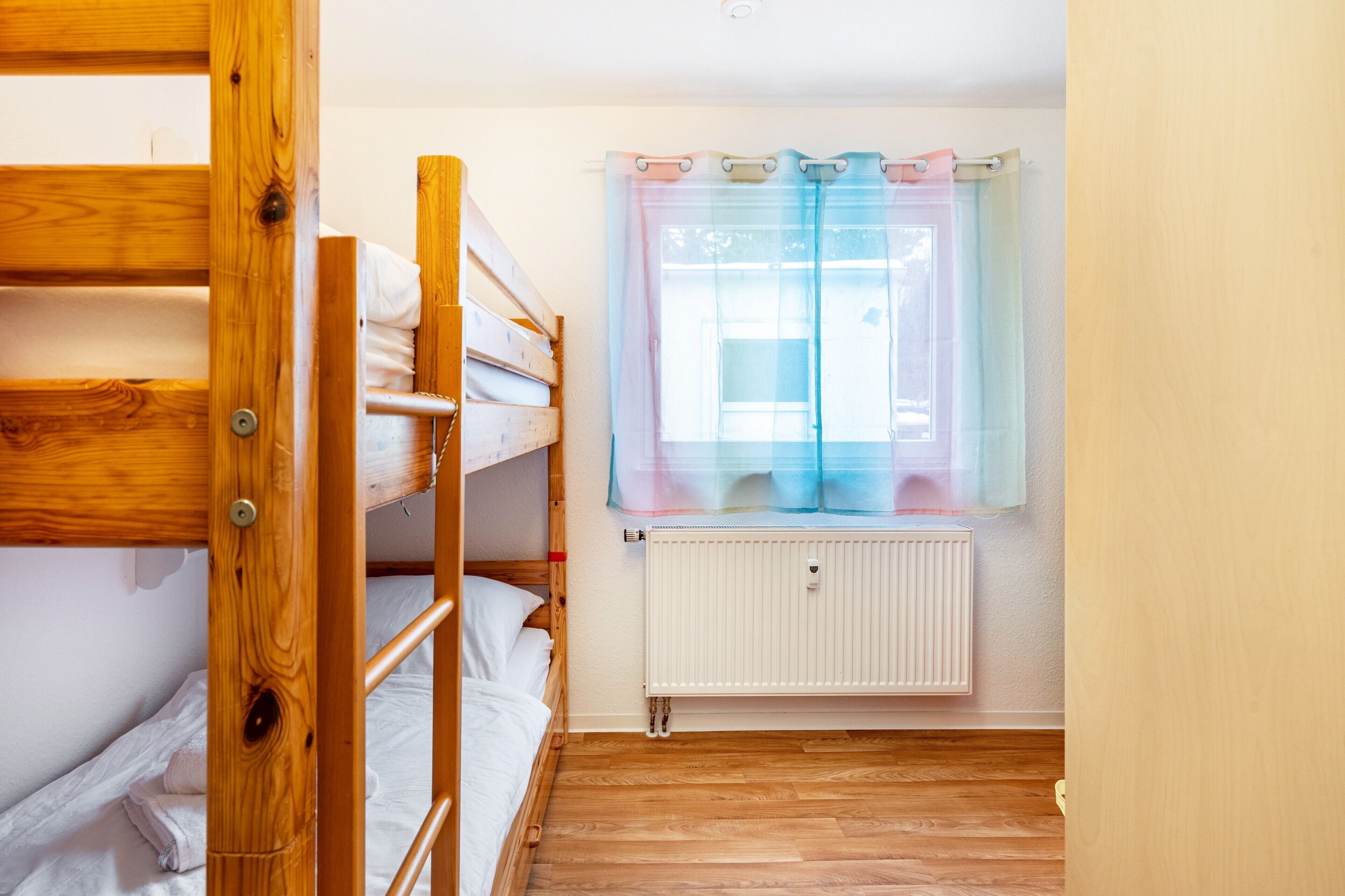 Ein Zimmer mit einem Etagenbett, einem Fenster mit Vorhang und einer Heizung.
