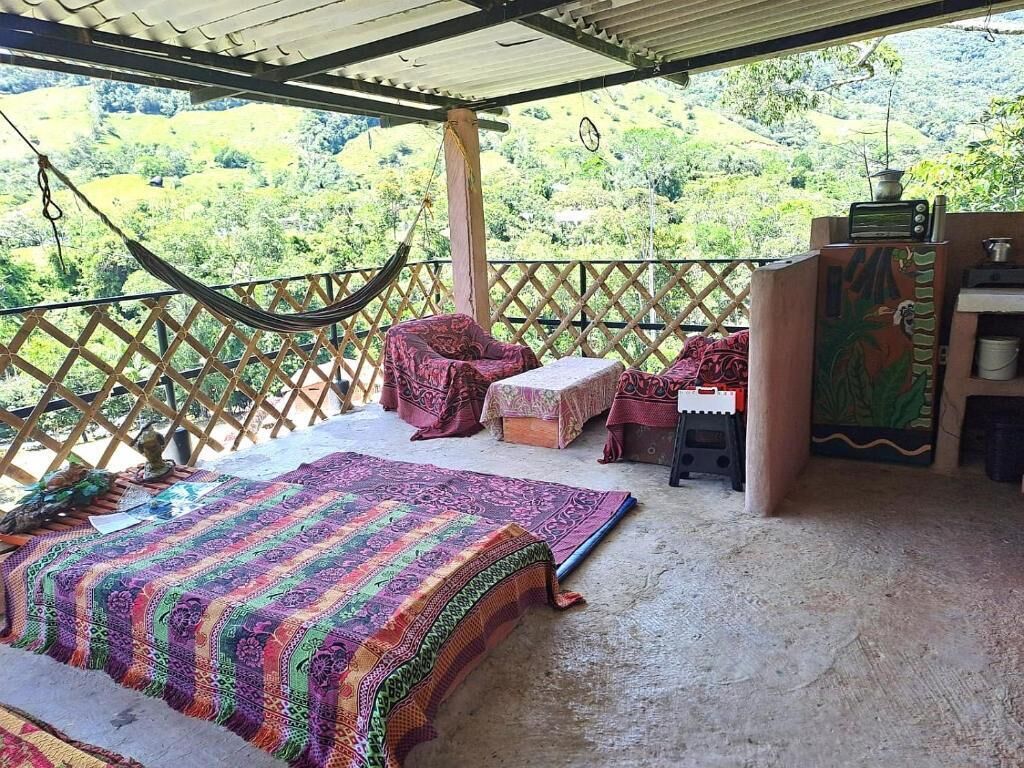 Une pièce avec un hamac, un lit recouvert d’une couverture colorée, une petite table et une vue sur un paysage luxuriant.