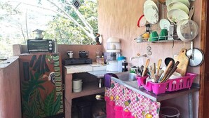 A compact kitchen with a microwave, coffee maker, and a shelf with dishes and utensils.