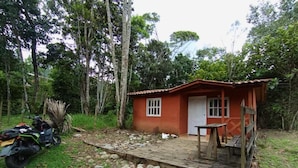 A small red wooden cabin with a porch, surrounded by trees and a stone pathway.
