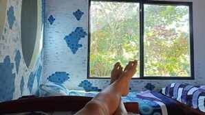 A bedroom with a bed, a window with a view of greenery, and a patterned wall.