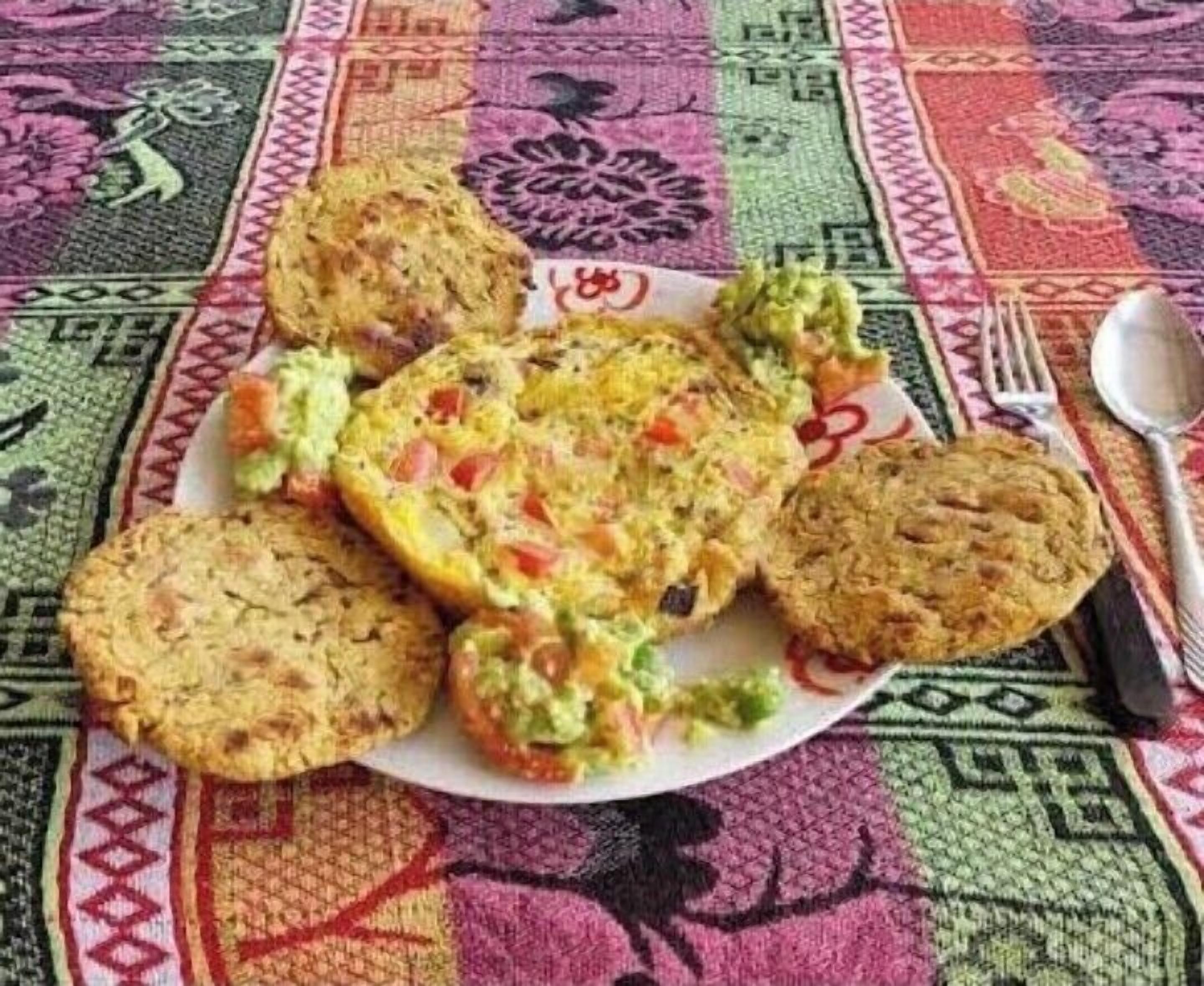 A plate with various food items, including a stuffed omelette, a slice of bread, and a muffin, on a colorful tablecloth.