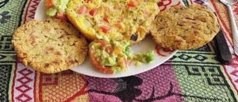 A plate with various food items, including a stuffed omelette, a slice of bread, and a muffin, on a colorful tablecloth.