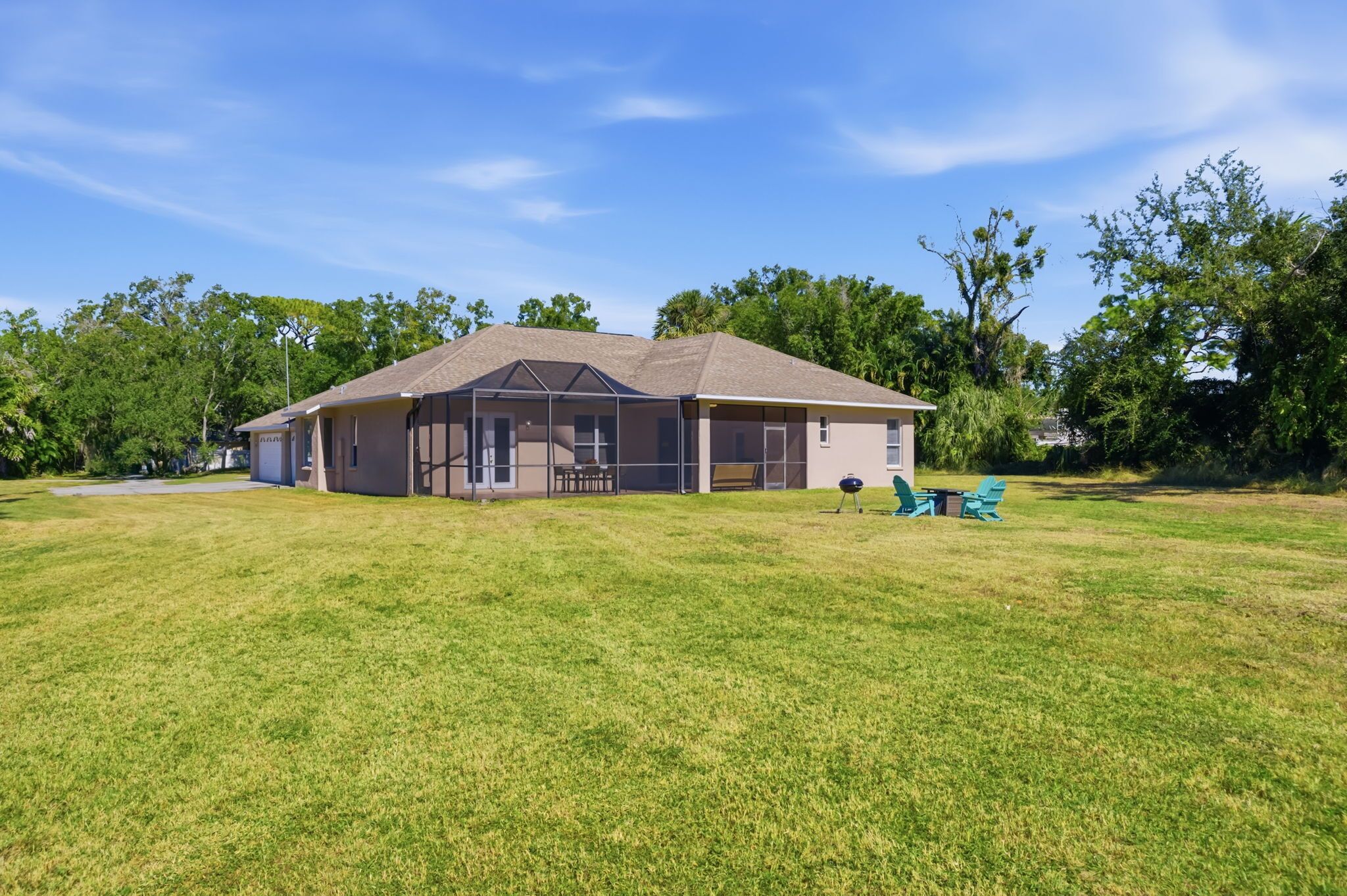 A single-story house with a covered patio area, a lawn, and trees in the background.