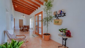 Une pièce spacieuse avec un plafond en bois, une plante en pot, une chaise, une table sur laquelle se trouve une cage à oiseaux, et une étagère fixée au mur, où sont posés des chapeaux et un sac.