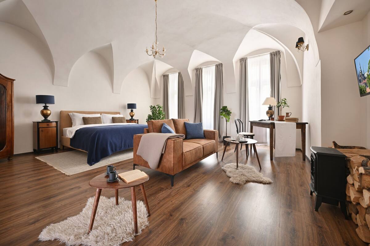 Una habitación amplia con una cama grande, un sofá marrón, una mesita redonda y una chimenea.