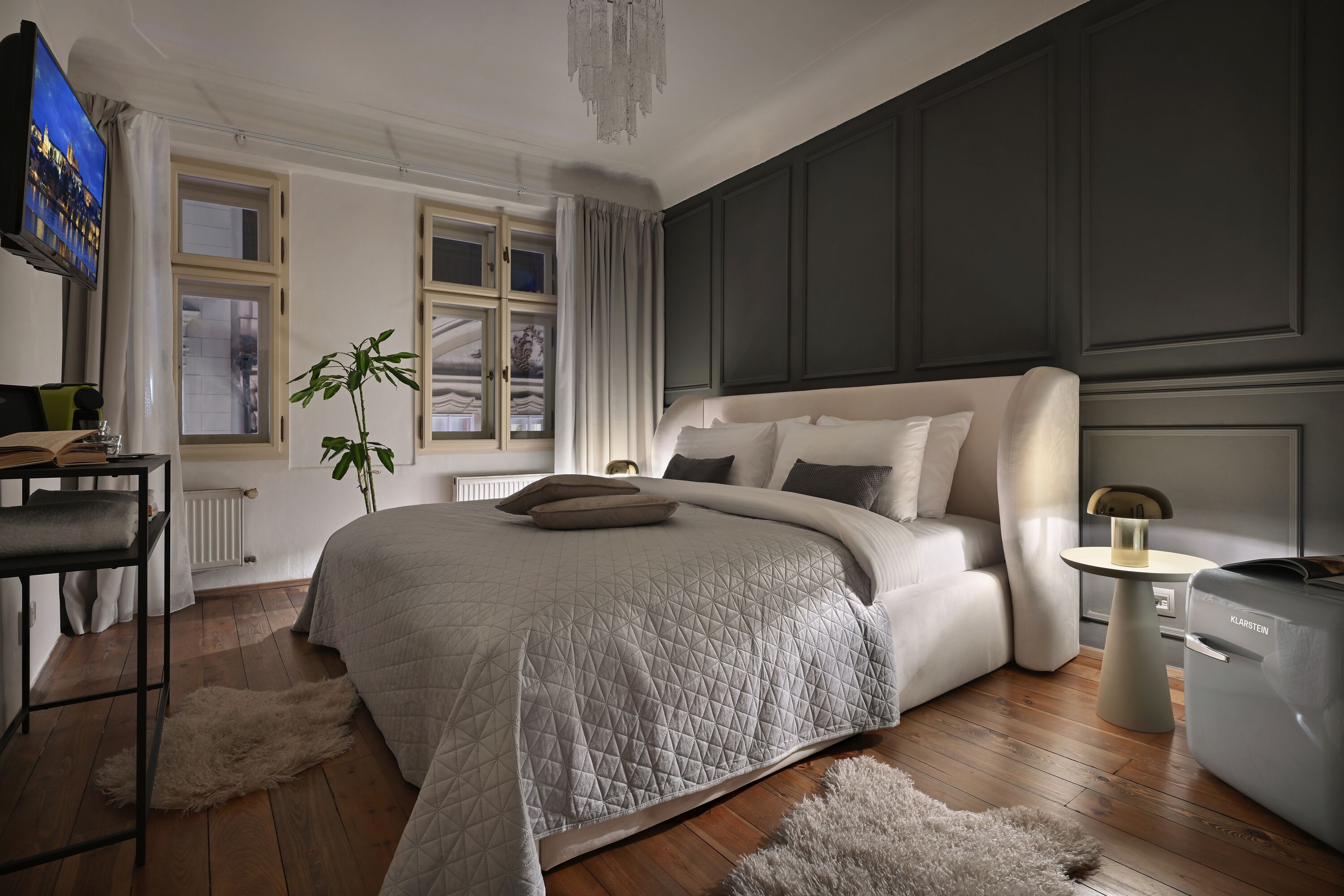 A modern bedroom with a large bed, a small table, a radiator, and a TV on the wall.