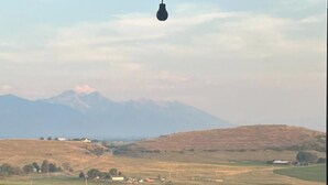 Vista de un paisaje rural con montañas al fondo, una carretera y algunos edificios.