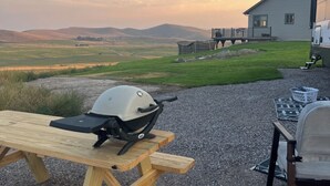 Un patio de grava con mesas de picnic y una parrilla.