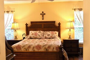 A bedroom with a wooden bed, floral bedding, two bedside lamps, a cross on the wall, and curtains on the windows. - 3/2 Designer in the Village of Hadley (The Villages)
