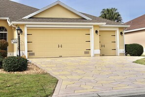 A two-car garage with a stone-patterned driveway, a small bush, and a street sign. - 3/2 Designer in the Village of Hadley (The Villages)