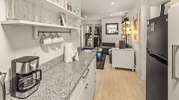 A modern kitchen with granite countertops, a coffee maker, and a refrigerator. There are shelves with glasses and a hanging rack for cups. - Prime Main Street location in Breckenridge (Breckenridge)