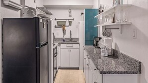 A compact kitchen with a black refrigerator, white cabinets, a granite countertop, and a teal accent wall. - Prime Main Street location in Breckenridge (Breckenridge)