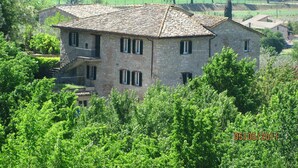 A stone building with a tiled roof, surrounded by lush greenery and fields. - Ostello della Pace Assisi (Assisi)