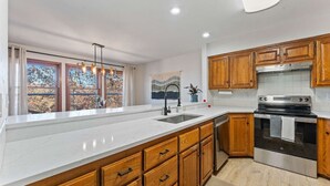 A modern kitchen with wooden cabinets, a stainless steel oven, and a large window with a view of trees. - Tunnel Vision Trail House Bike In Bike Out (Bella Vista)