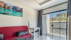 A modern room with a red sofa, a small white table, and a painting of a lake. - Apt w/ 1 Bedroom and Air Conditioning Irn0103 (Florianópolis)