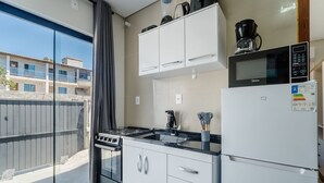 A modern kitchen with a gas stove, microwave, and refrigerator. There is a window with a view of buildings outside. - Apt w/ 1 Bedroom and Air Conditioning Irn0103 (Florianópolis)