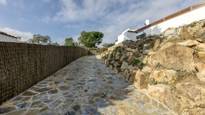 Un sendero de piedra que lleva a un edificio blanco con valla de madera y muros de piedra.