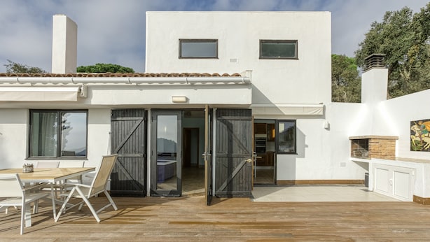 Una casa moderna con un patio, un comedor y una cocina visibles a través de puertas abiertas.