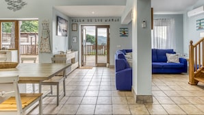 Amplia sala de estar con un sofá azul, una mesa de comedor de madera y una cocina visible a través de una puerta abierta.