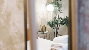 Una camera d'albergo con un letto, una lampada, uno specchio e una pianta.