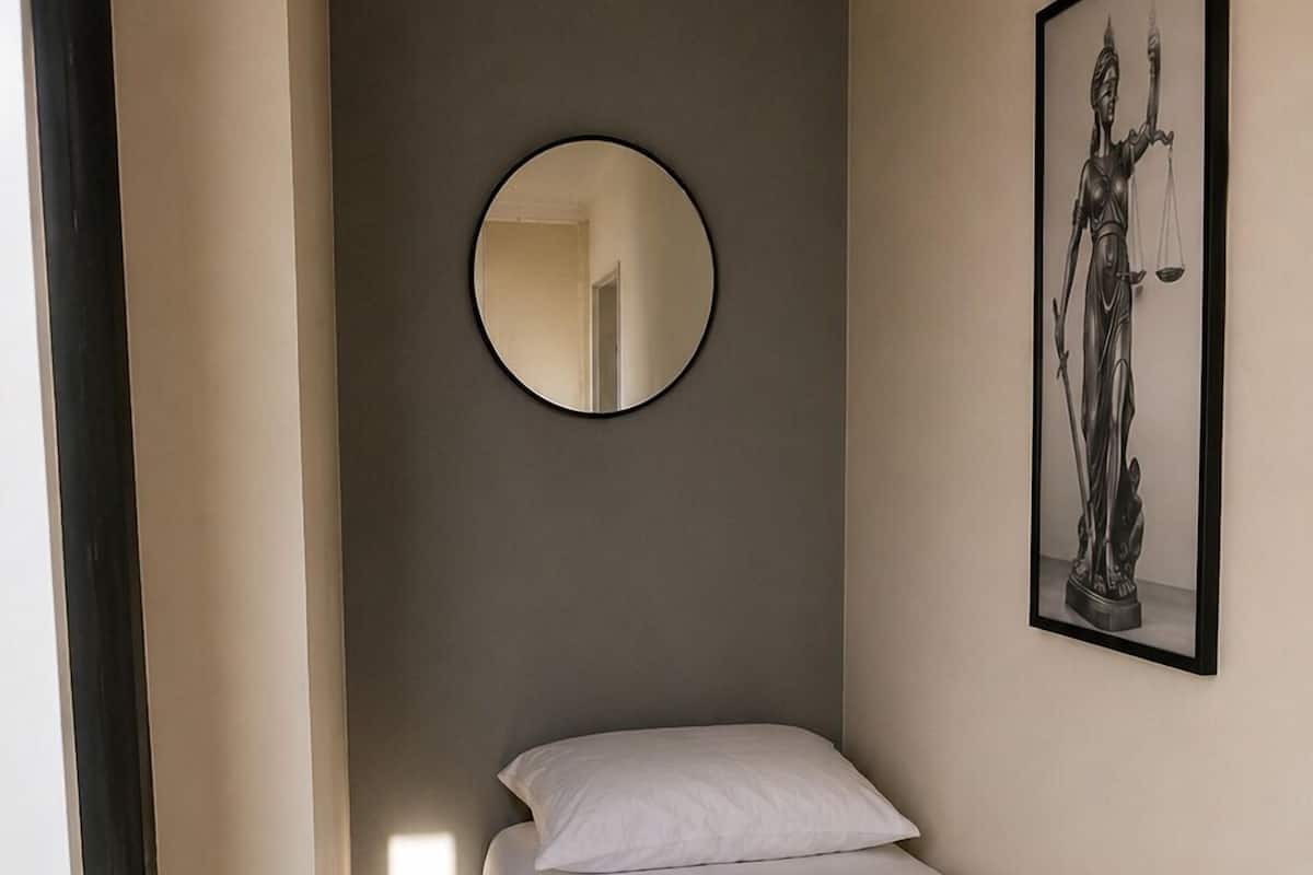 A bedroom with a bed, a round mirror, and a framed artwork on the wall.