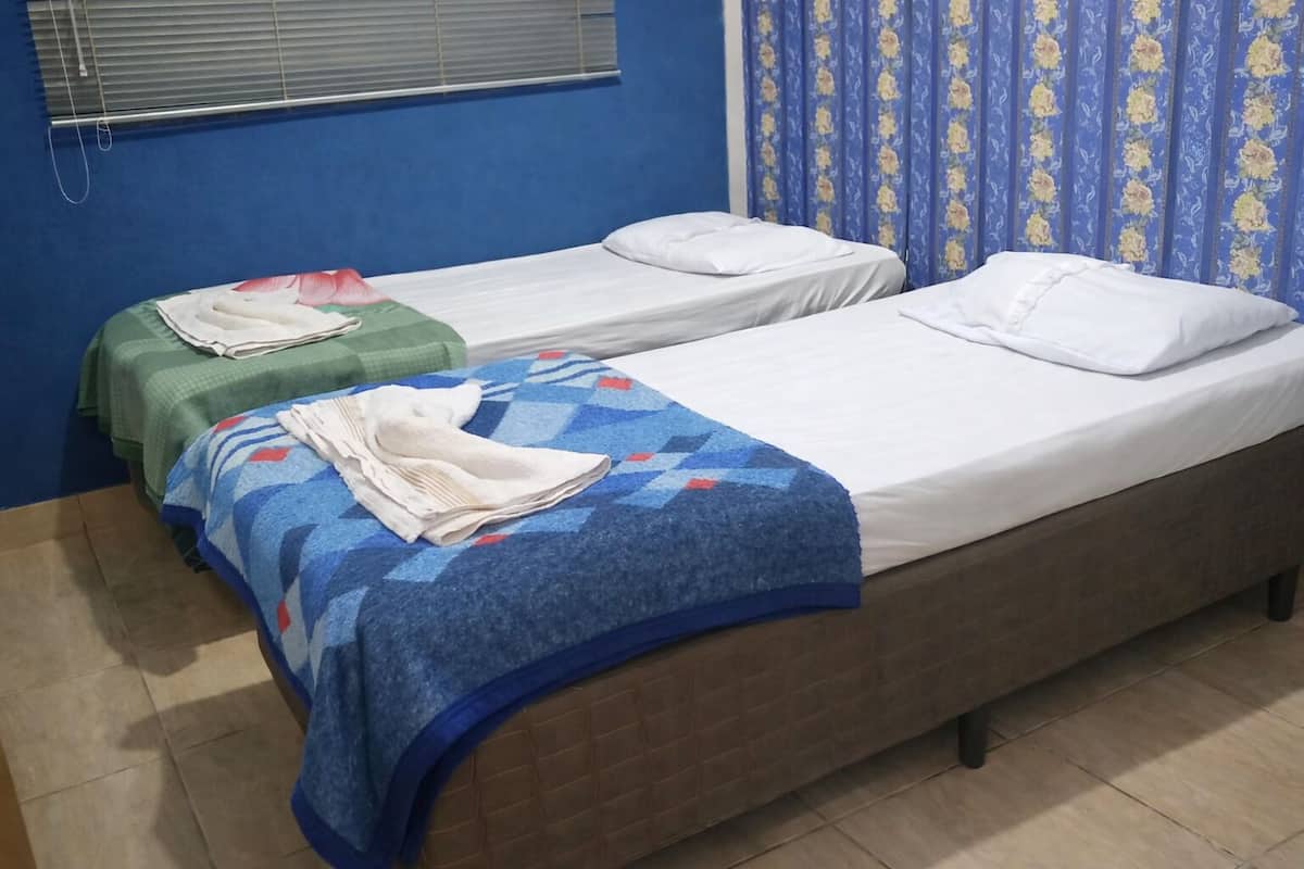 A room with two single beds, a window with blinds, and a curtain with a floral pattern.