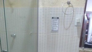 Un baño con inodoro, cabina de ducha, suelo de baldosas y un pequeño cubo de basura.