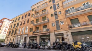 A multi-story building with balconies, a row of parked scooters, and a storefront with a closed shutter. - Sea View Central Apartment by Wonderful Italy (Sanremo)