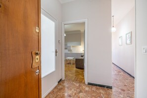 A hallway with a wooden door, a white door, and a kitchen area with a dining table and a sofa. - Sea View Central Apartment by Wonderful Italy (Sanremo)