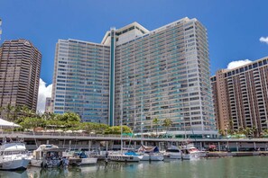 A high-rise hotel with multiple balconies, a marina with boats, and a clear blue sky. - 7th Fl Ilikai | AC | Pool (Honolulu)