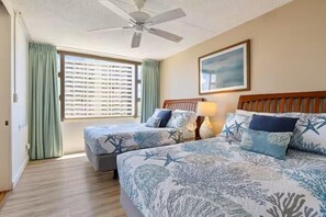 Ein Hotelzimmer mit zwei Betten, einem Deckenventilator, einem Fenster mit Jalousien und einem gerahmten Bild an der Wand.