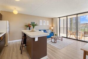 Eine moderne Wohnung mit einer Küchenzeile, einem Wohnbereich mit Sofa und Couchtisch sowie einem Balkon mit Gartenmöbeln.