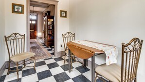 Uma sala de jantar com piso xadrez, uma mesa com toalha florida e duas cadeiras.