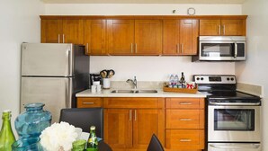 A compact kitchen with wooden cabinets, stainless steel appliances, and a granite countertop. - 29th Fl Waikiki Banyan | Diamond Head Views | Parking | AC (Honolulu)