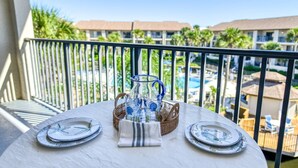 A table set with plates, a pitcher, and a basket on a balcony overlooking a pool and resort buildings. - Ocean Villas #126 (St. Augustine)