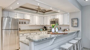 A modern kitchen with white cabinetry, stainless steel appliances, a granite countertop, and a central island with bar stools. - Ocean Villas #126 (St. Augustine)