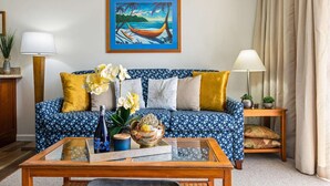 Ein Wohnzimmer mit einem gemusterten Sofa, einem Glastisch und einem Bild von einem Boot am Strand.