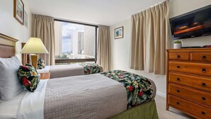 Ein Hotelzimmer mit zwei Betten, einem Fernseher, einem Schminktisch und einem Fenster mit Blick auf die Stadt.
