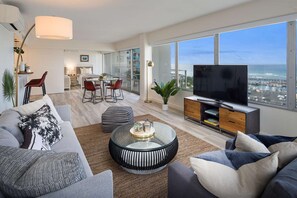 Una sala de estar moderna con un televisor grande, asientos cómodos, un comedor y vista al océano.