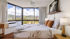 Une chambre d’hôtel avec un grand lit, un ventilateur de plafond, une vue sur la ville et un tableau accroché au mur.