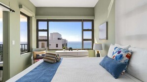 Ett hotellrum med en stor säng, utsikt över havet och en balkong med utsikt över byggnaderna.