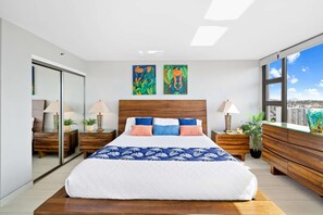 Un dormitorio moderno con una cama grande, cabecera de madera, dos cuadros, vista a la ciudad y una puerta de cristal.
