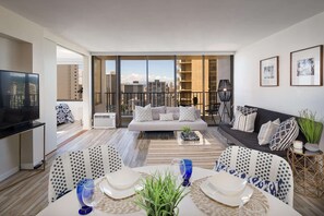 Ein modernes Wohnzimmer mit einer Couch, einem Esstisch und Stühlen, einem Fernseher und einem Balkon mit Blick auf die Stadt.